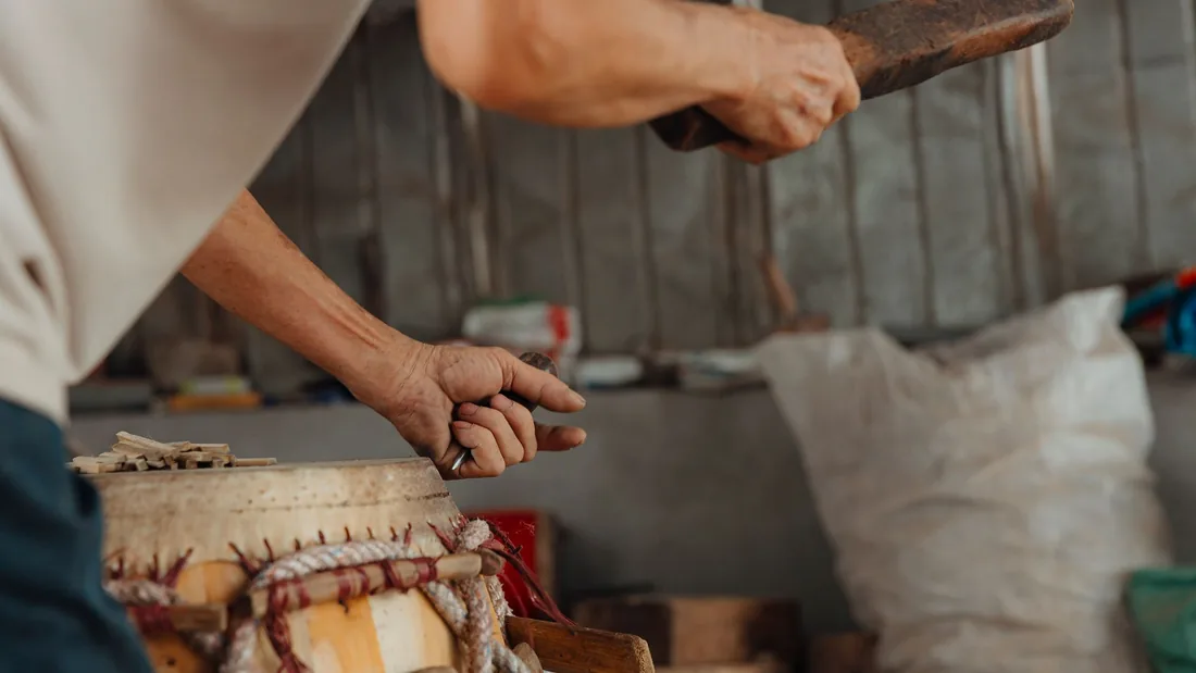 Manos de un artesano trabajando con mazo y gubia sobre el casco de un tambor en un taller